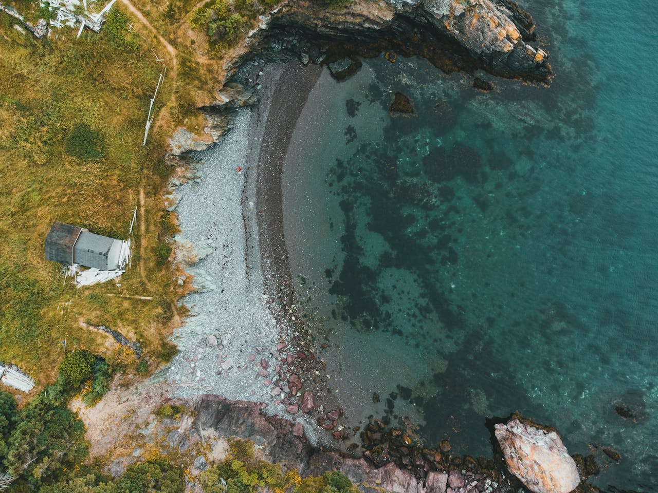 Aerial shot capturing a calm coastline with rocky shores and clear blue waters.